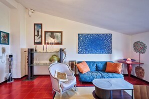 Ein Wohnzimmer mit einer Couch, einem Sessel und einem Couchtisch. An den Wänden hängen Bilder in Rahmen und auf einem Beistelltisch steht eine Zierdekoration.