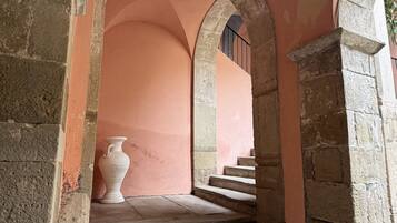 Un corridoio in pietra con archi, un vaso e una scala.