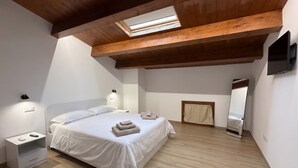 A bedroom with a sloped ceiling, a skylight, a bed with white bedding, a bedside table with a lamp, a mirror, and a wooden floor. - Holiday home in the historic centre of Fuscaldo Paese (Fuscaldo)