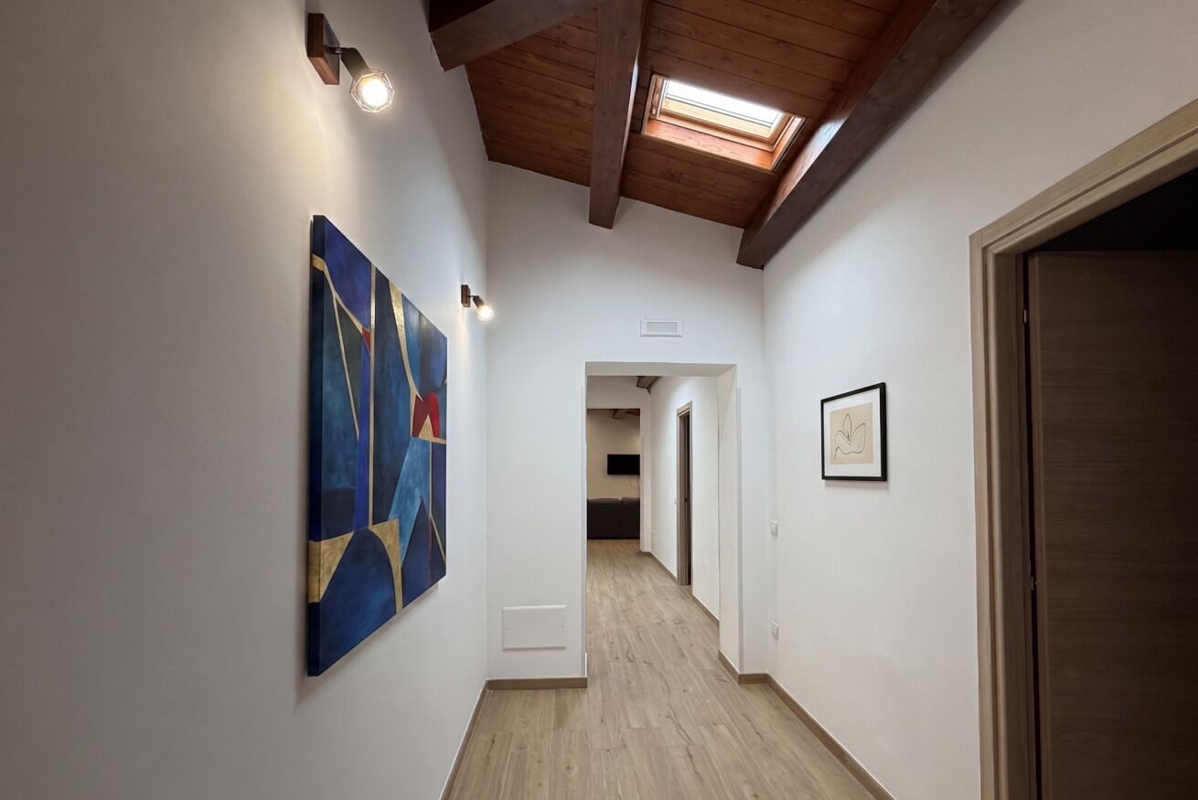 Un corridoio con una finestra a soffitto, travi in legno, un quadro e una fotografia incorniciata al muro.