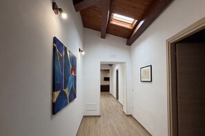 Un corridoio con una finestra a soffitto, travi in legno, un quadro e una fotografia incorniciata al muro.