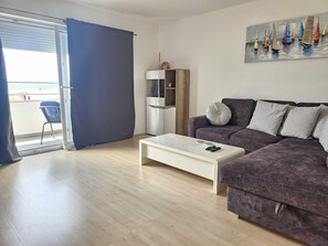 Ein modernes Wohnzimmer mit einer Couch, einem Couchtisch, einer TV-Konsole und einem Gemälde mit Segelbooten.