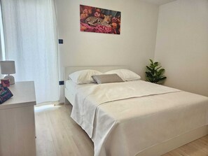 Ein Schlafzimmer mit Bett, Nachttisch, Lampe, einer Pflanze und einem Bild an der Wand.