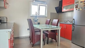Pieni, käytännöllinen keittiö, jossa on ruokapöytä, tuolit, jääkaappi ja ikkuna.