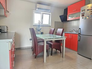 Eine kleine Küche mit Esstisch, Stühlen, einem Kühlschrank und einem Fenster.