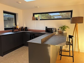 A modern kitchen with a large island, a microwave, and a toaster. - Birdsong (Penzance)