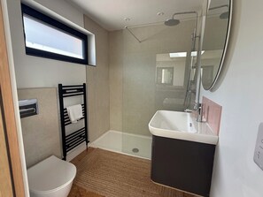 Ein modernes Badezimmer mit Toilette, Handtuchhalter, Duschkabine, Waschbecken und Spiegel.