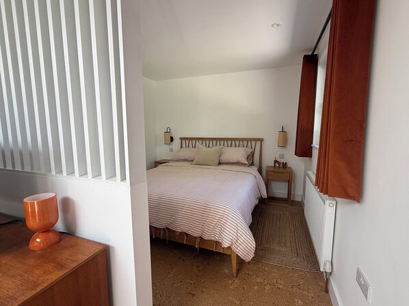 Un dormitorio con cama, mesitas de noche, radiador y una ventana con persianas.