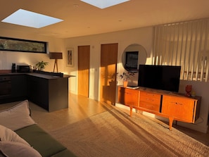 A modern living space with a kitchen, a dining area, a green sofa, a wooden TV stand, and a skylight. - Birdsong (Penzance)
