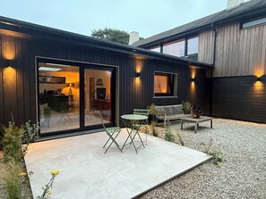 Ein modernes Haus mit Terrasse, einer Schiebetür und einem kleinen Tisch mit Stühlen.