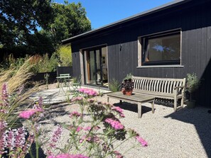 A modern building with a wooden bench and potted plants in the foreground. - Birdsong (Penzance)