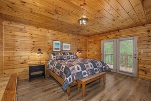 Ein Schlafzimmer in einer Holzhütte mit Bett, Sitzbank, Nachttischen und einer Tür mit Aussicht.