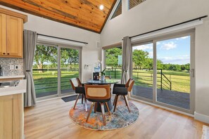 A dining area with a round table, four chairs, and a view of a green landscape through large sliding doors. - Luxury Ranch Retreat, Hot Tub, Private Fishing Pond, Longhorns, Sleeps 6 (Bonham)