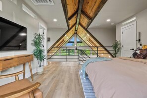 A bedroom with a sloped ceiling, a bed, a desk, and a TV. - Luxury Ranch Retreat, Hot Tub, Private Fishing Pond, Longhorns, Sleeps 6 (Bonham)