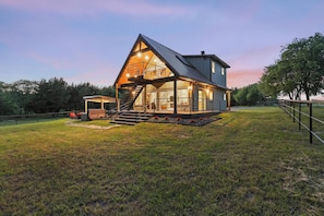 A modern house with a large glass facade, a prominent staircase, and a well-maintained lawn. - Luxury Ranch Retreat, Hot Tub, Private Fishing Pond, Longhorns, Sleeps 6 (Bonham)
