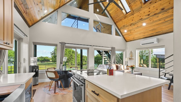A spacious kitchen with a large island, a dining area with a table and chairs, and a view of the outdoors through large windows.