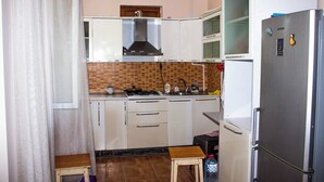 Uma cozinha compacta com armários brancos, geladeira de aço inoxidável, fogão a gás e painel de azulejos.