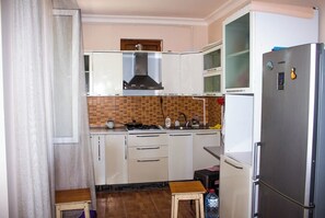 Eine kleine Küche mit weißen Schränken, einem Edelstahlkühlschrank, einem Gasherd und einer gefliesten Spritzschutzwand.