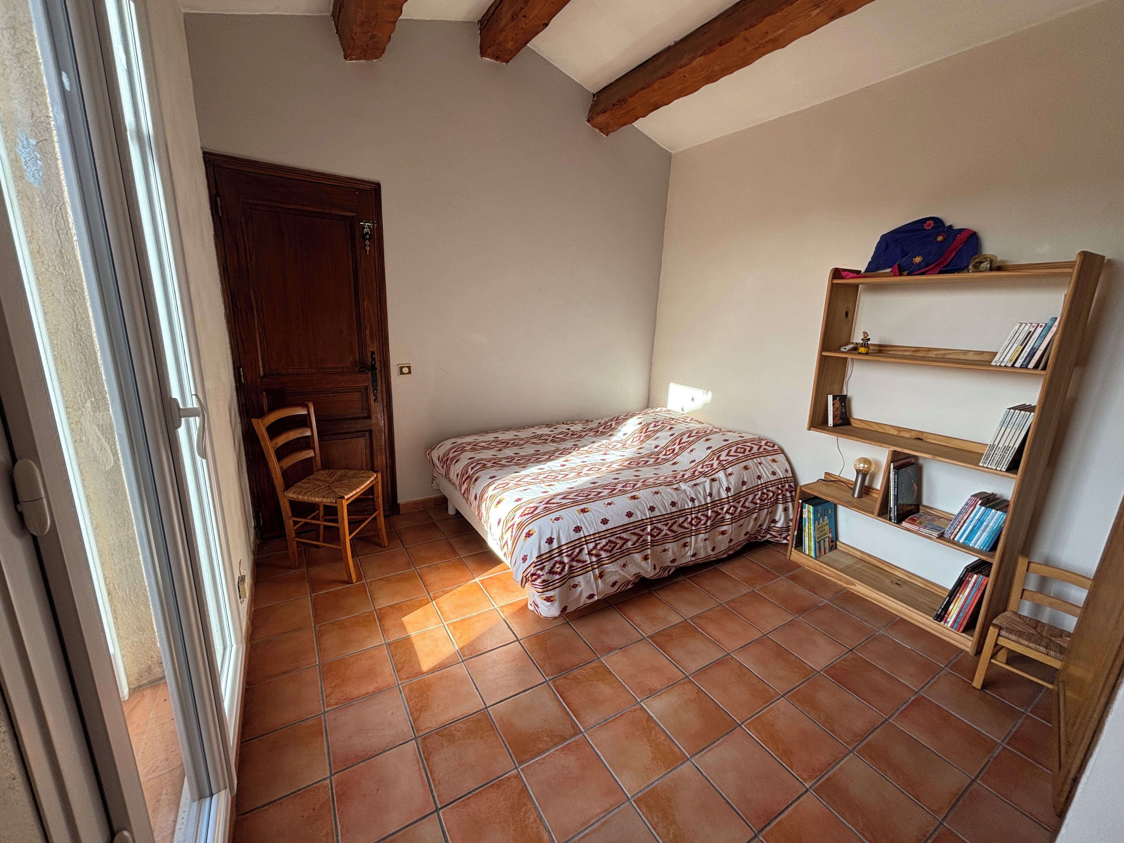 Een slaapkamer met een bed, een houten stoel, een boekenkast en een deur.