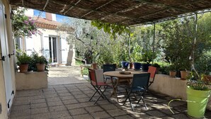 Eine Terrasss mit Tisch und Stühlen, umgeben von Kübelpflanzen und einer Pergola.