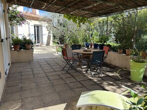 Une terrasse extérieure avec une table et des chaises, entourée de plantes en pot et agrémentée d’une pergola.