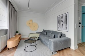 En moderne stue med en grå sofa, et rundt træbord, en grå måtte og et billede i ramme på væggen.
