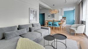 Un soggiorno moderno con un divano grigio, una zona pranzo con sedie blu e una cucina sullo sfondo.