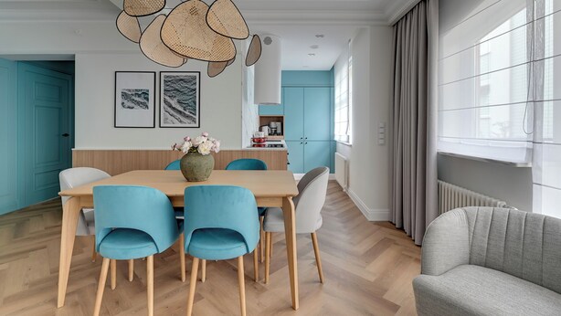 Un'area pranzo moderna con tavolo in legno, sedie blu e lampadario intrecciato.
