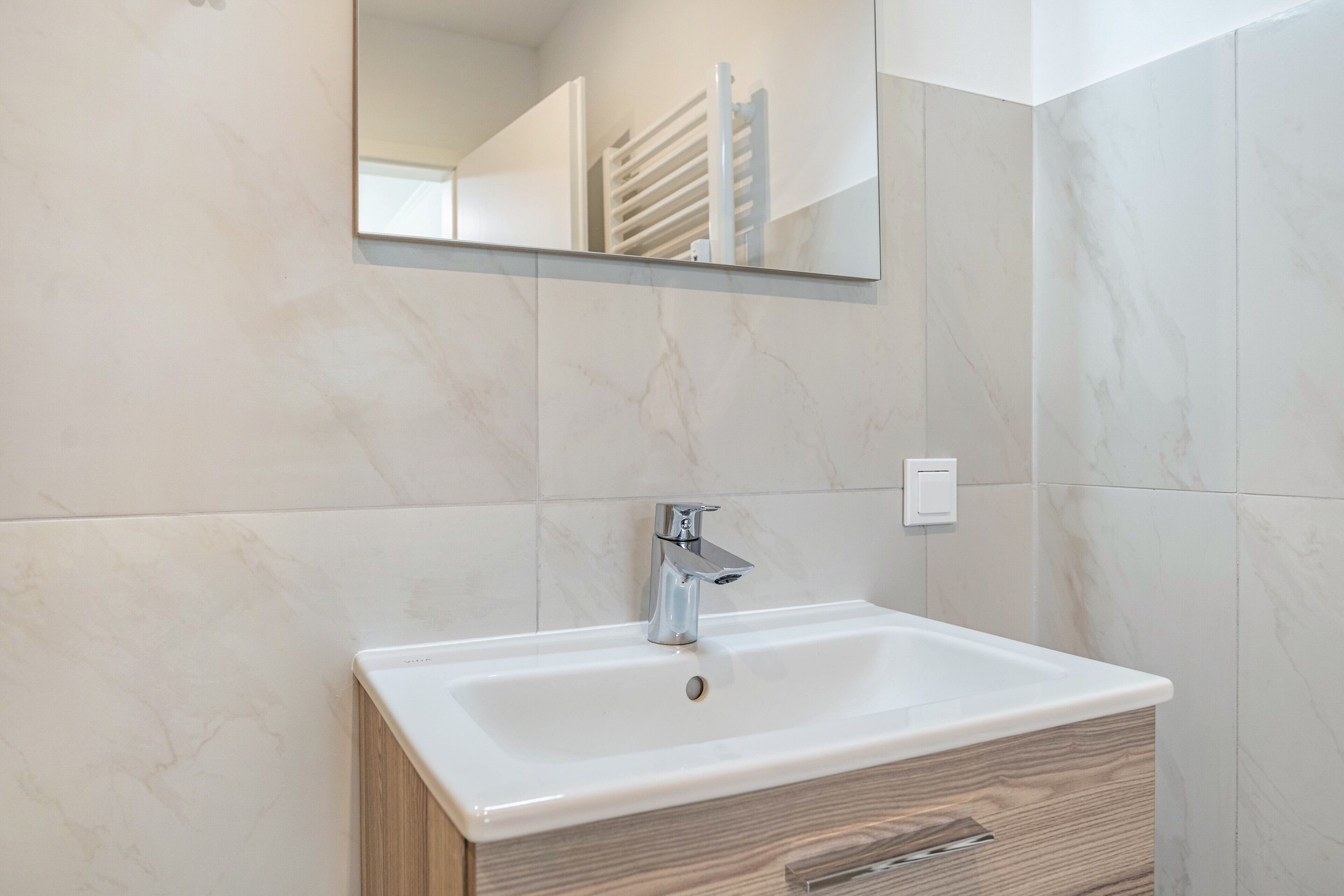 A bathroom with a white sink, a mirror above it, and marble walls.