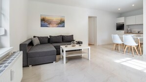 A modern living room with a gray sofa, a white coffee table, and a painting on the wall. - Apartment 'Whg 1.1 EG Links Vorn' with Private Terrace and Wi-Fi (Putbus)