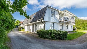A two-story house with a sloped roof, a covered porch, and a driveway leading to the entrance. - Apartment 'Whg 1.1 EG Links Vorn' with Private Terrace and Wi-Fi (Putbus)