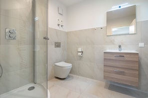 A modern bathroom with a glass shower enclosure, a toilet, and a vanity with drawers.