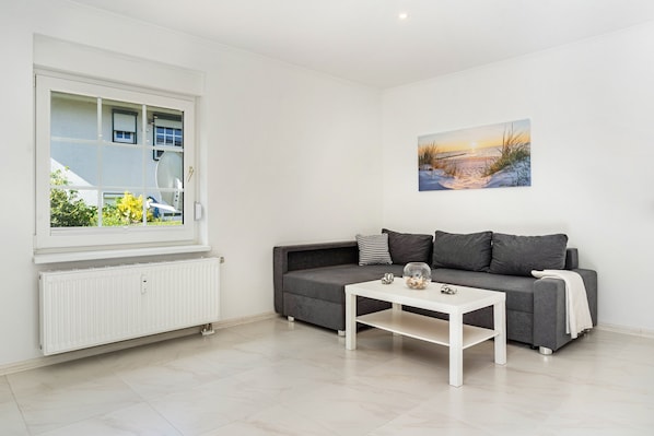 A modern living room with a grey sofa, white coffee table, and a painting of a beach scene.