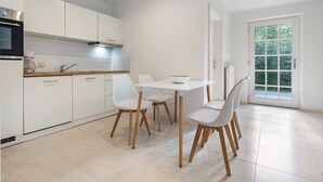 A modern kitchen with white cabinets, a dining table with chairs, and a large window with a view of greenery. - Apartment 'Whg 1.1 EG Links Vorn' with Private Terrace and Wi-Fi (Putbus)