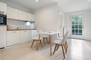A modern kitchen with white cabinets, a dining table with chairs, and a large window with a view of greenery.