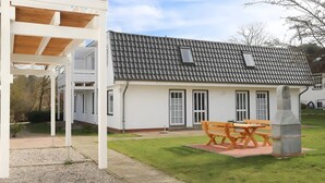 Ein modernes Haus mit Ziegeldach, einer überdachten Veranda mit Holzbanken und einem gepflegten Rasen.