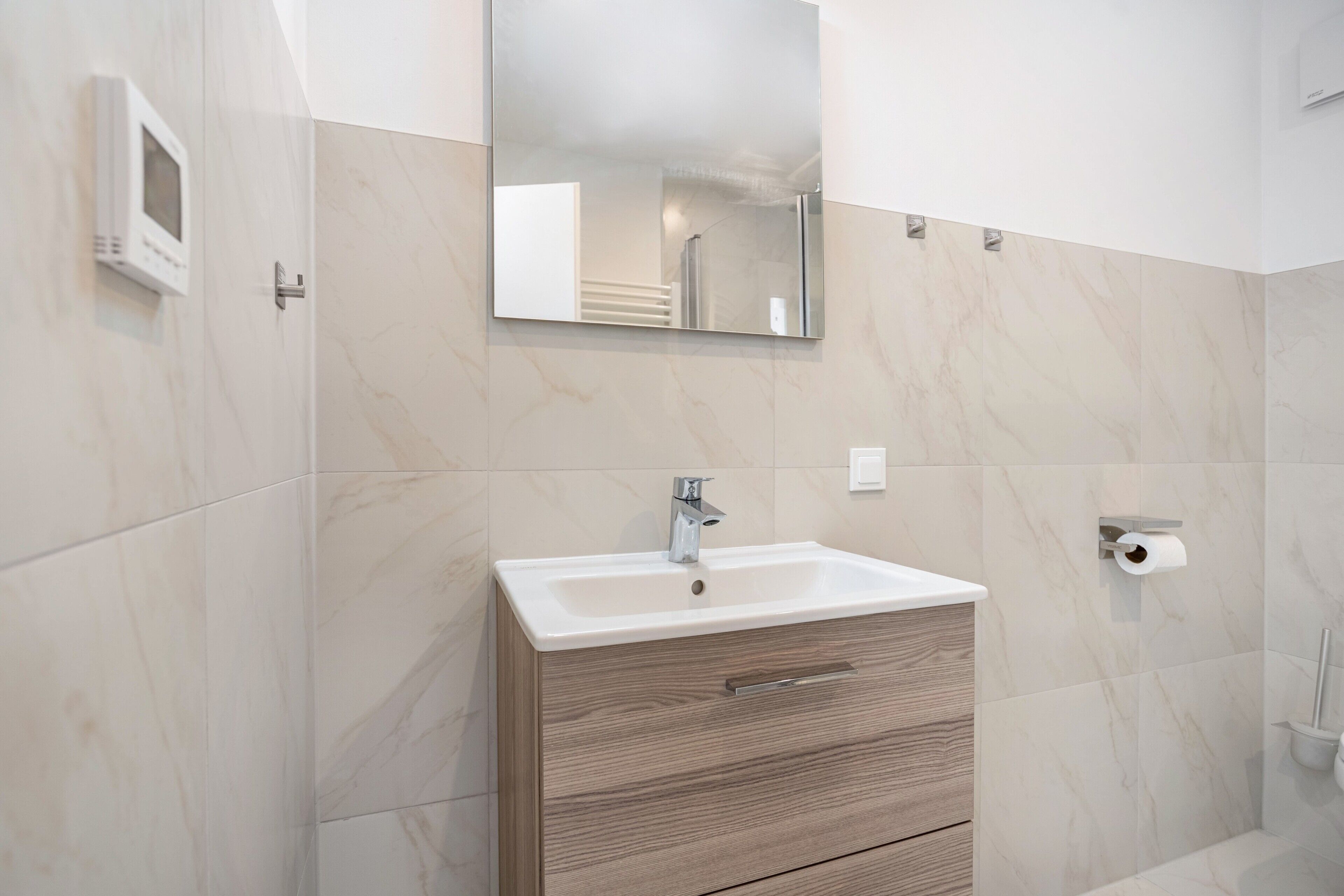 A bathroom with a marble wall, a sink with a mirror, and a toilet paper holder.