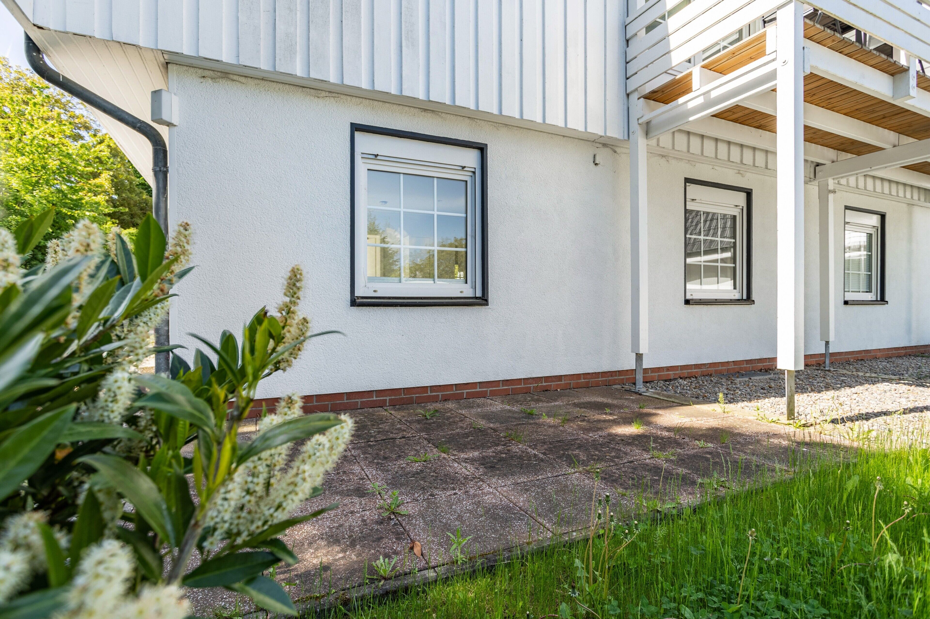 Een gebouw met een witte gevel, een overdekte veranda en een kleine tuin met planten.