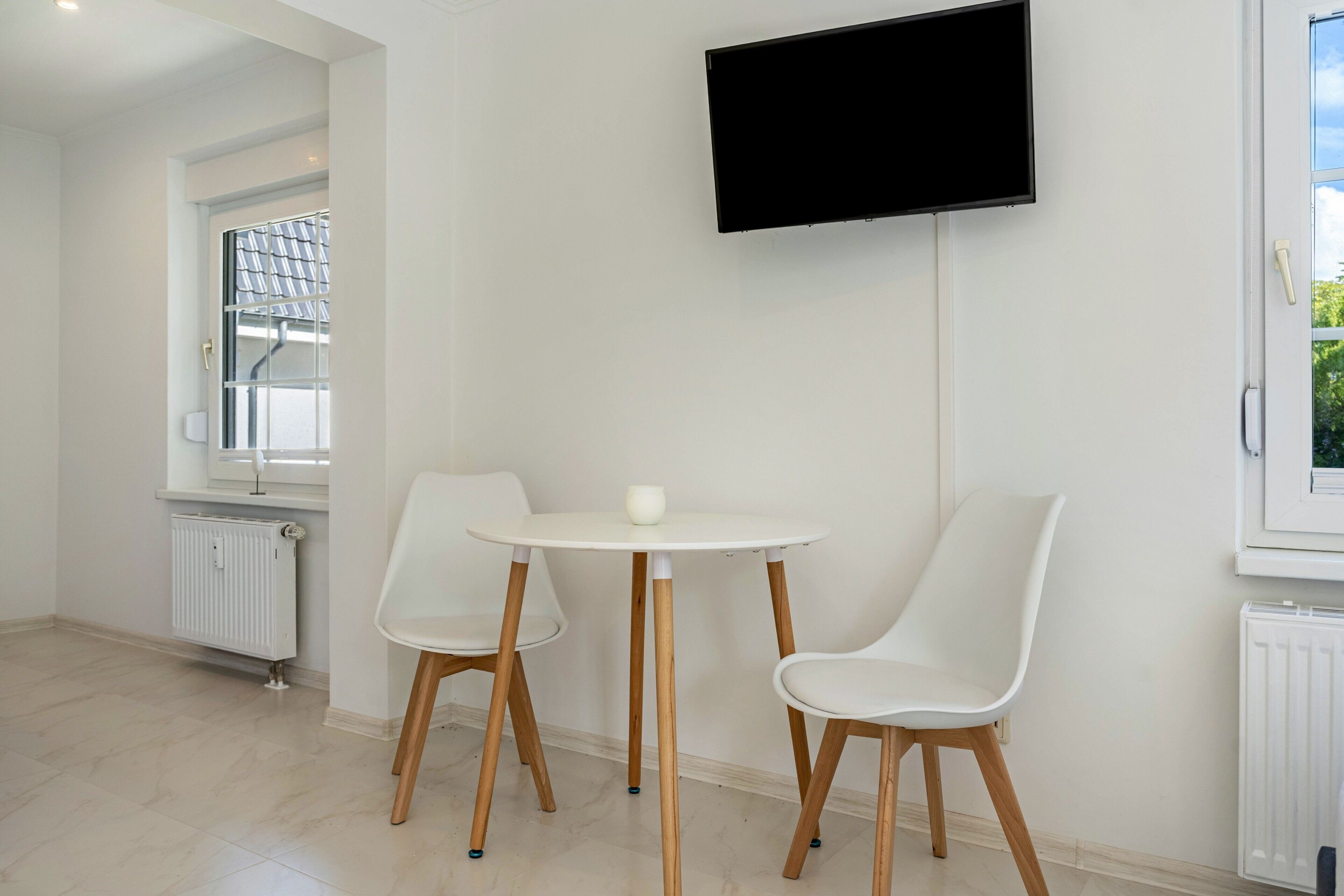 Une chambre moderne avec une table blanche et deux chaises, un téléviseur fixé au mur et une fenêtre donnant sur un beau paysage.