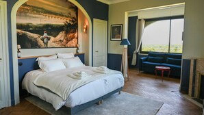 Une chambre avec un grand lit, un tableau au-dessus du lit, un canapé et une vue par la fenêtre.