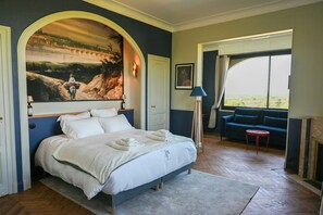 Een slaapkamer met een groot bed, een schilderij erboven, een bank en uitzicht door een raam.