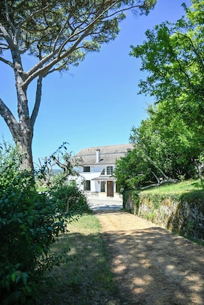 A house with a paved driveway leading to a white building with a tiled roof.