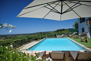 Piscina con vista sulla campagna, circondata dal verde e da un ombrellone bianco.