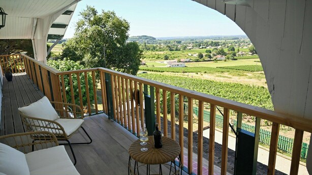 Un balcon avec vue sur les vignes, des meubles en osier et une bouteille de vin.