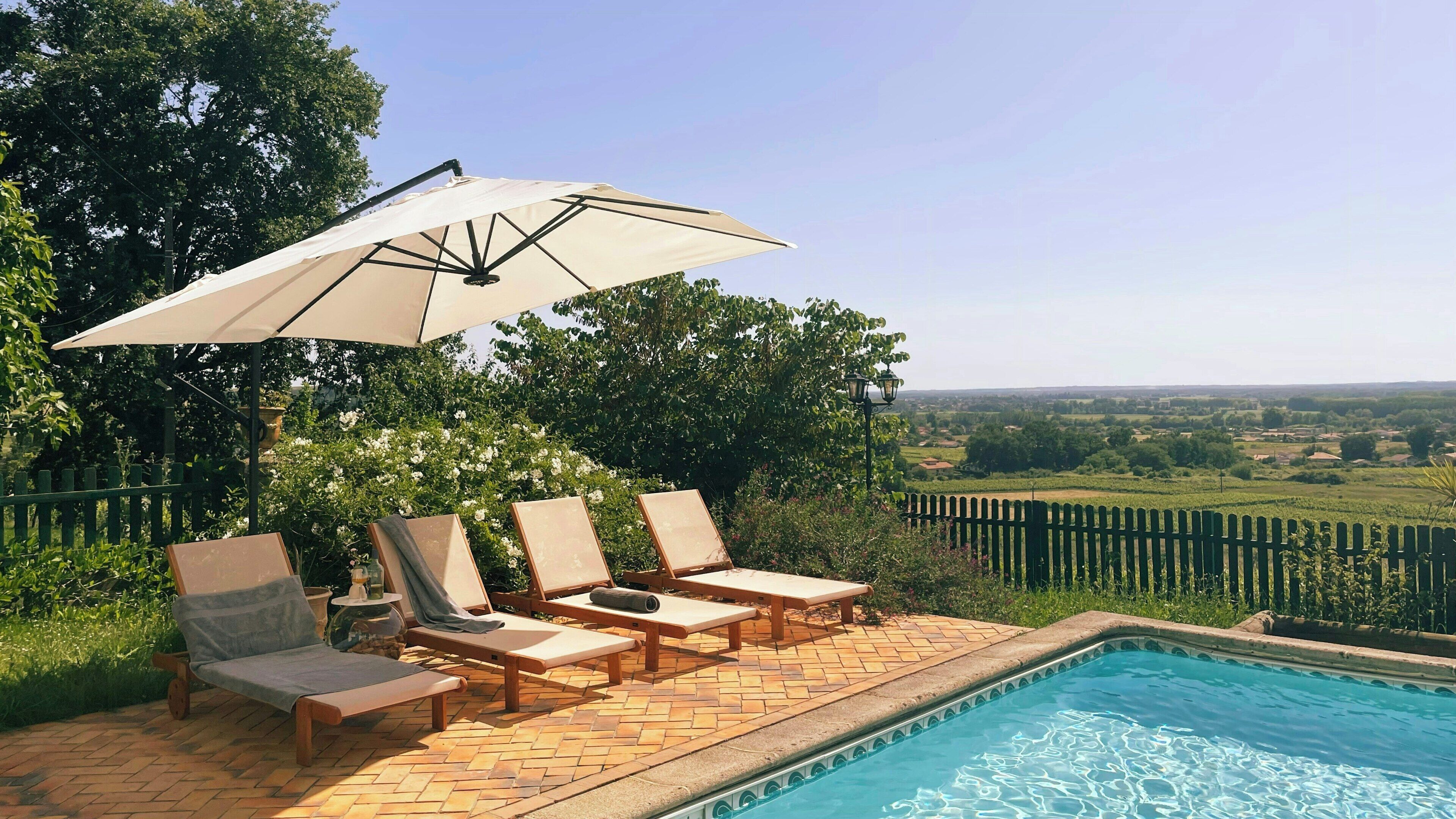 A poolside area with lounge chairs, an umbrella, and a view of the countryside.