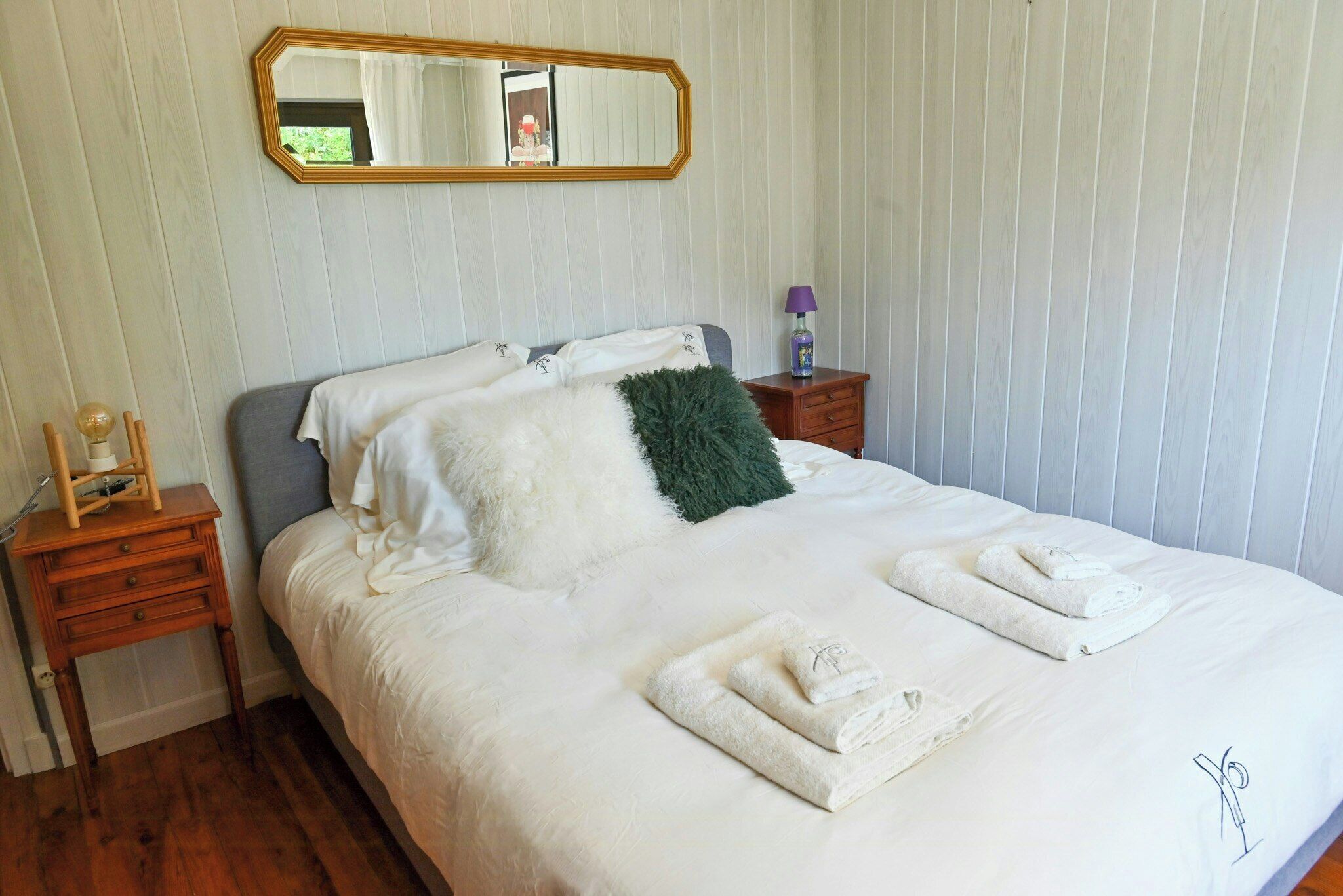 A neatly made bed with white linens, a green throw pillow, and rolled towels on the side.
