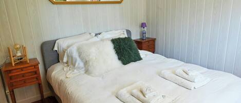 A neatly made bed with white linens, a green throw pillow, and rolled towels on the side.