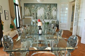 Een eetruimte met een glazen tafel en stoelen, een fles wijn en een behang met patroon.