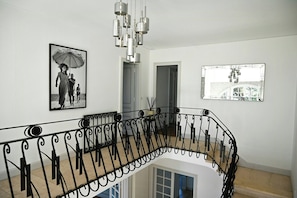 A staircase with ornate black railings, a black and white photograph, and a modern chandelier.