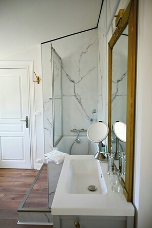 Un bagno con un lavandino bianco, uno specchio, una doccia e una parete in marmo.